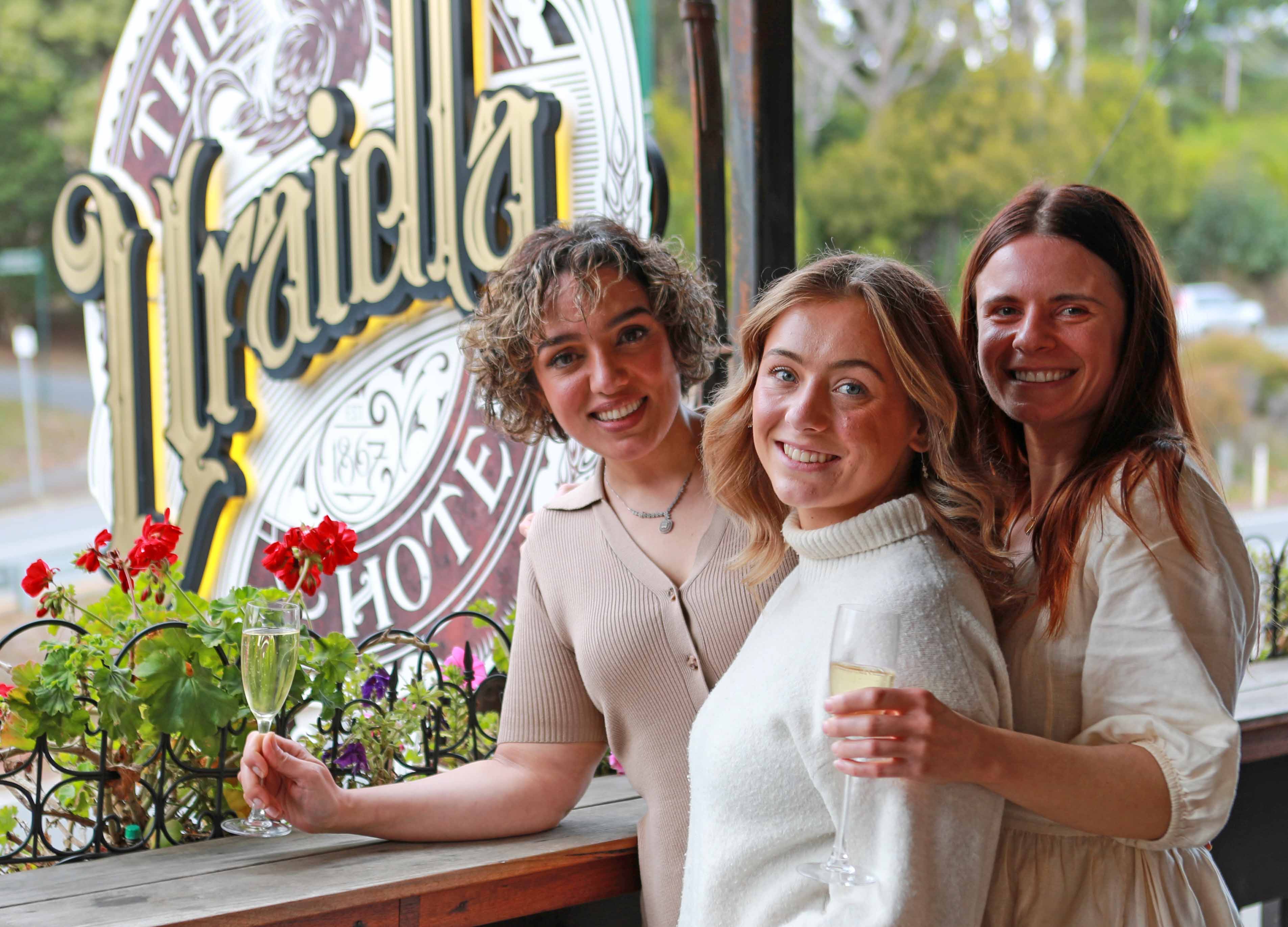 Three friends with drinks at a window bearing the Uraidla Hotel sign